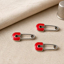 Dije esmaltado, en forma de gancho con color rojo base plateado, 26 x 12 mm, por unidad