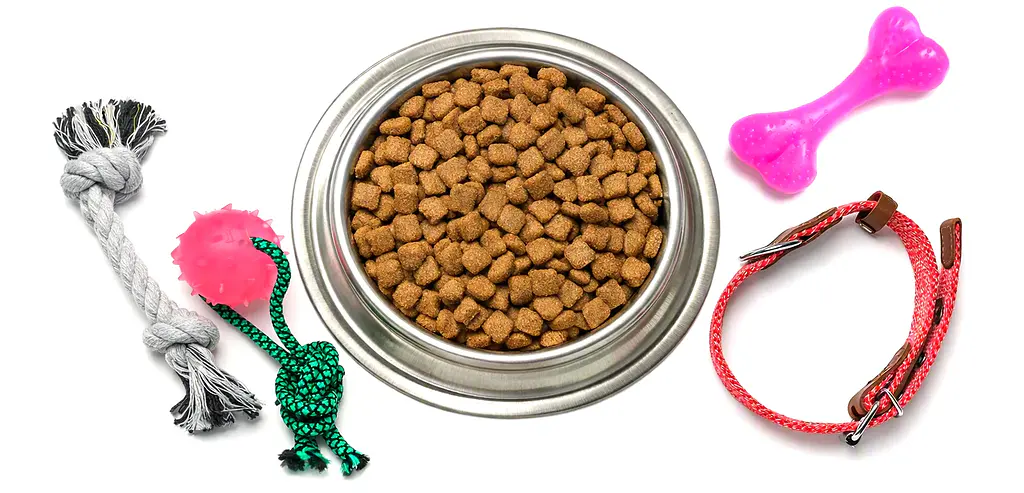 Plato de pellets para perro con accesorios y juguetes de goma color rosa y verde alrededor.