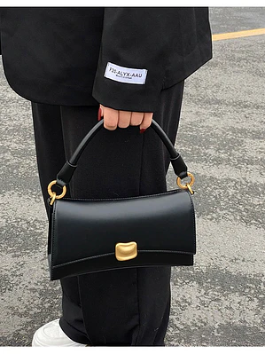 Bolso de hombro negro con cierre dorado y asa rígida — estilo urbano minimalista