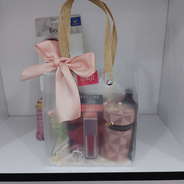 Saco plástico pequeno com laço rosa, batom Maybelline, carteirinha redonda e pincel maquiagem.